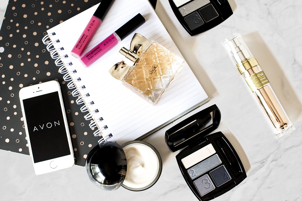 makeup and avon luck fragrance on a desk with a note book
